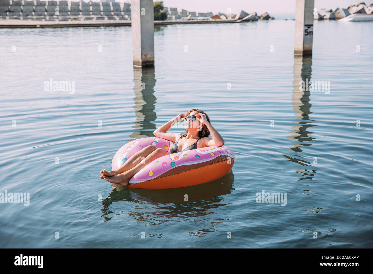Jeune femme se baignant dans la mer sur flotteur gonflable en forme de beigne Banque D'Images