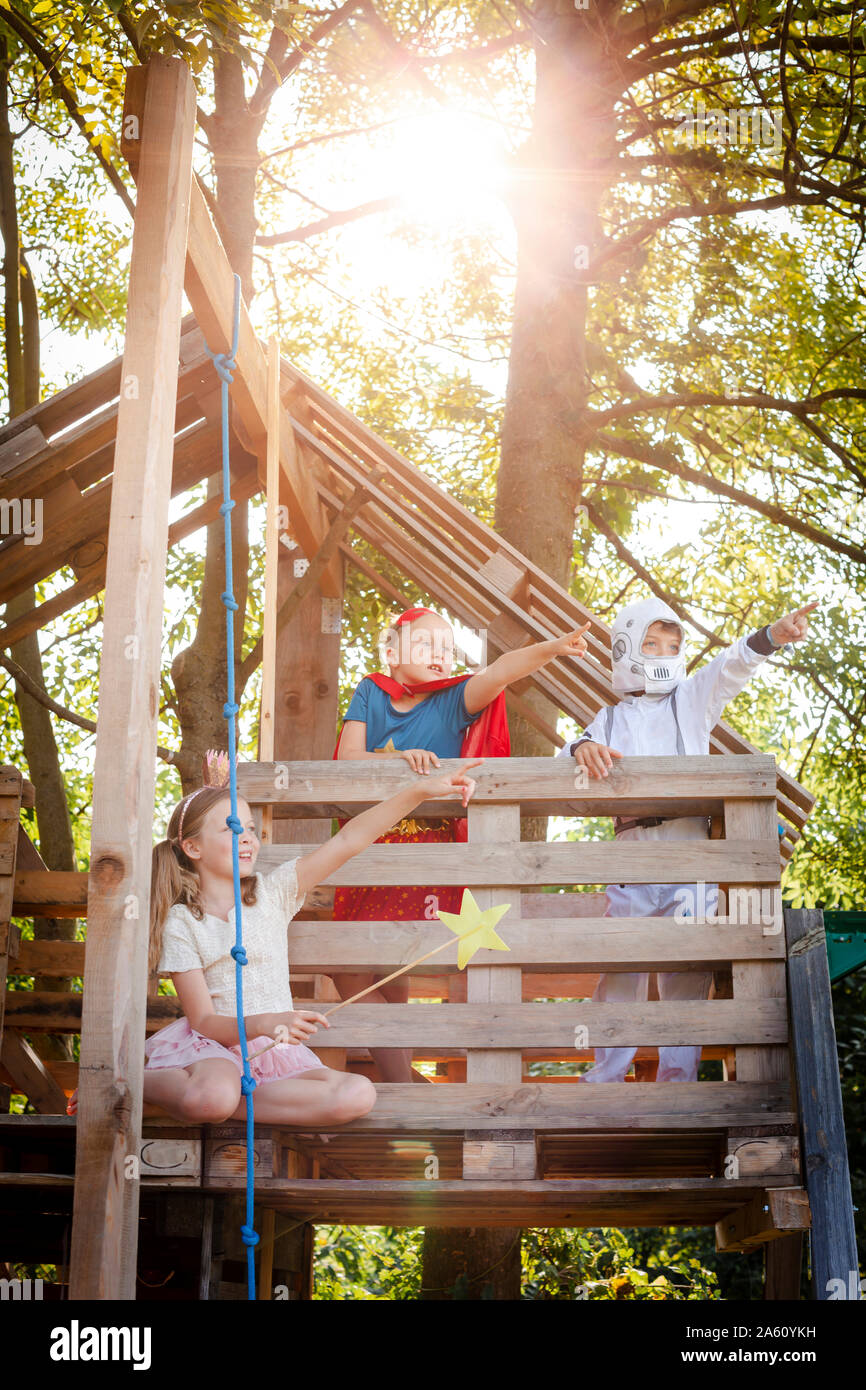 Trois enfants avec des costumes de super-héros jouant sur leur maison de l'arbre Banque D'Images