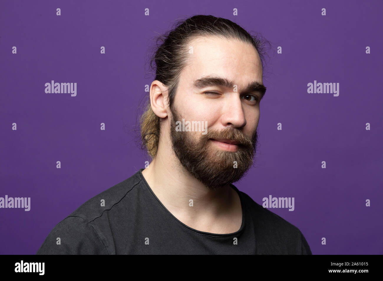 Portrait de jeune homme barbu avec un clin d'contre fond violet Banque D'Images