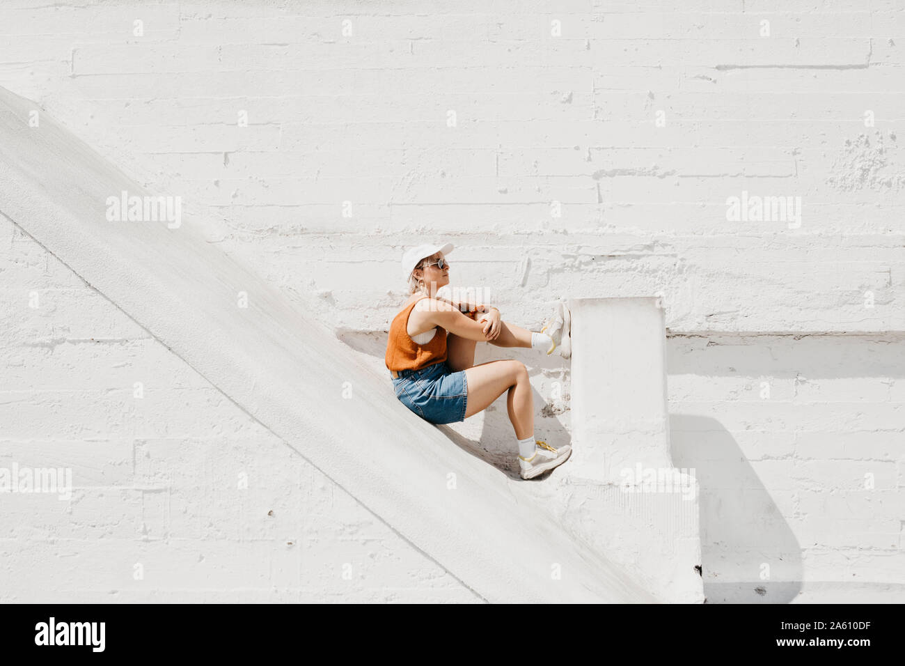 Jeune femme assise en face d'un mur blanc à l'extérieur Banque D'Images