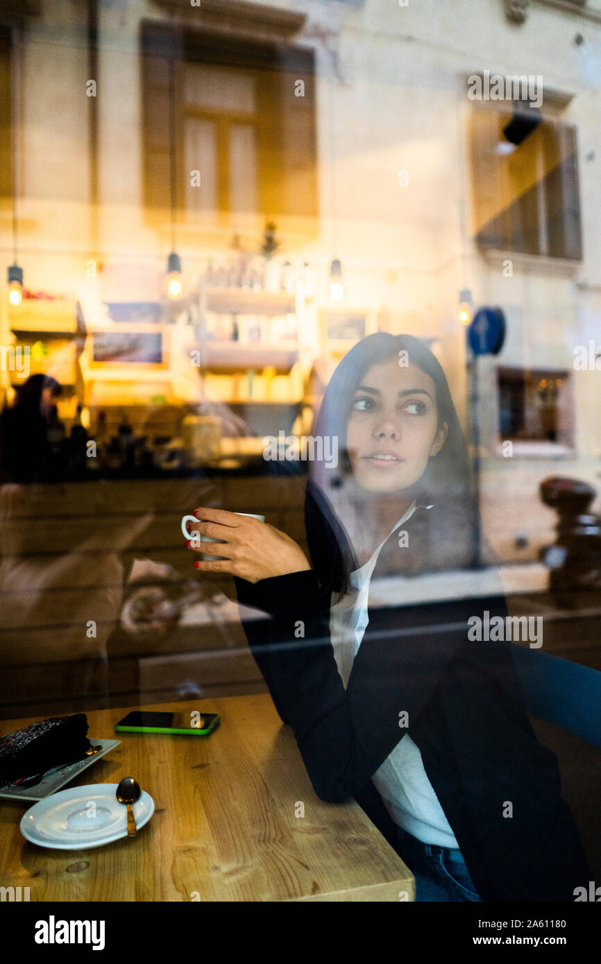 Jeune femme dans un café derrière la vitre Banque D'Images