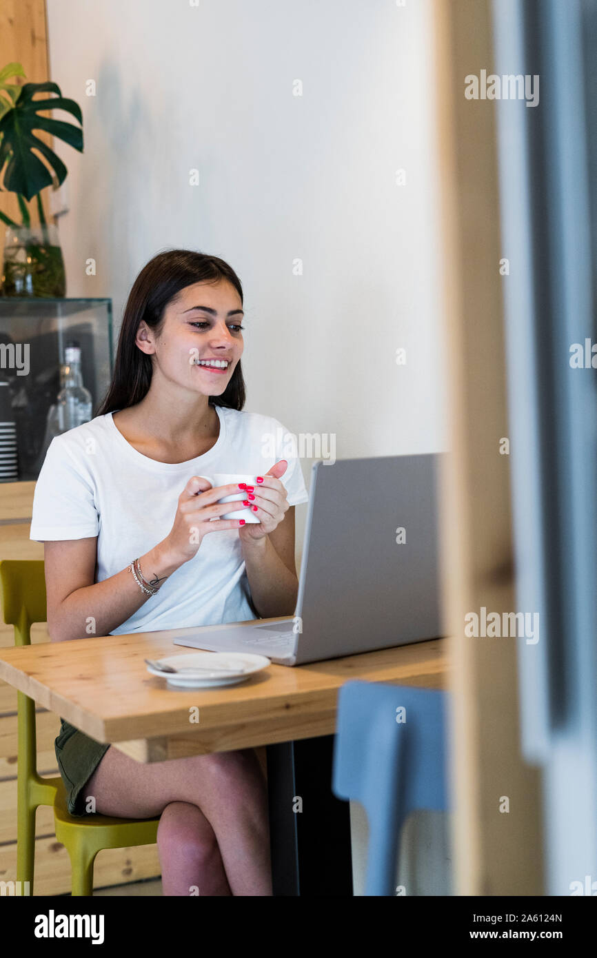 Smiling young woman using laptop in a cafe Banque D'Images