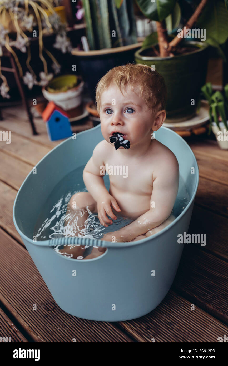 Baby Boy sitting in baby baignoire sur le balcon, jouer avec un jouet Banque D'Images