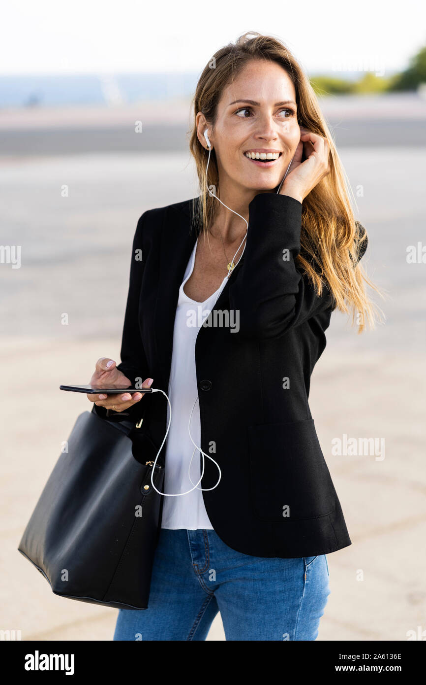 Happy businesswoman avec écouteurs et smartphone outdoors Banque D'Images