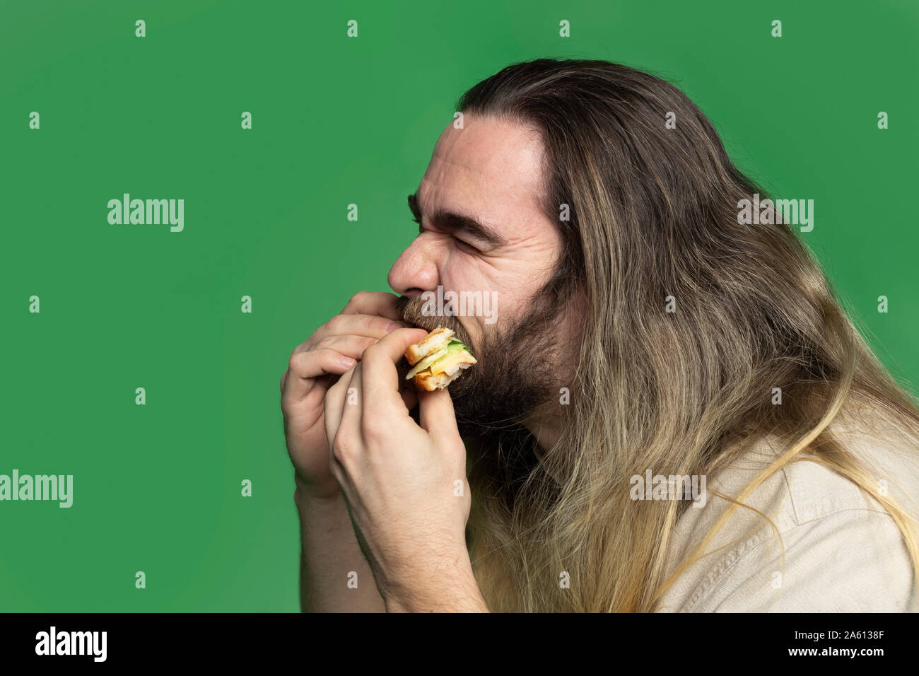 Bearded man eating sandwich en face de fond vert Banque D'Images