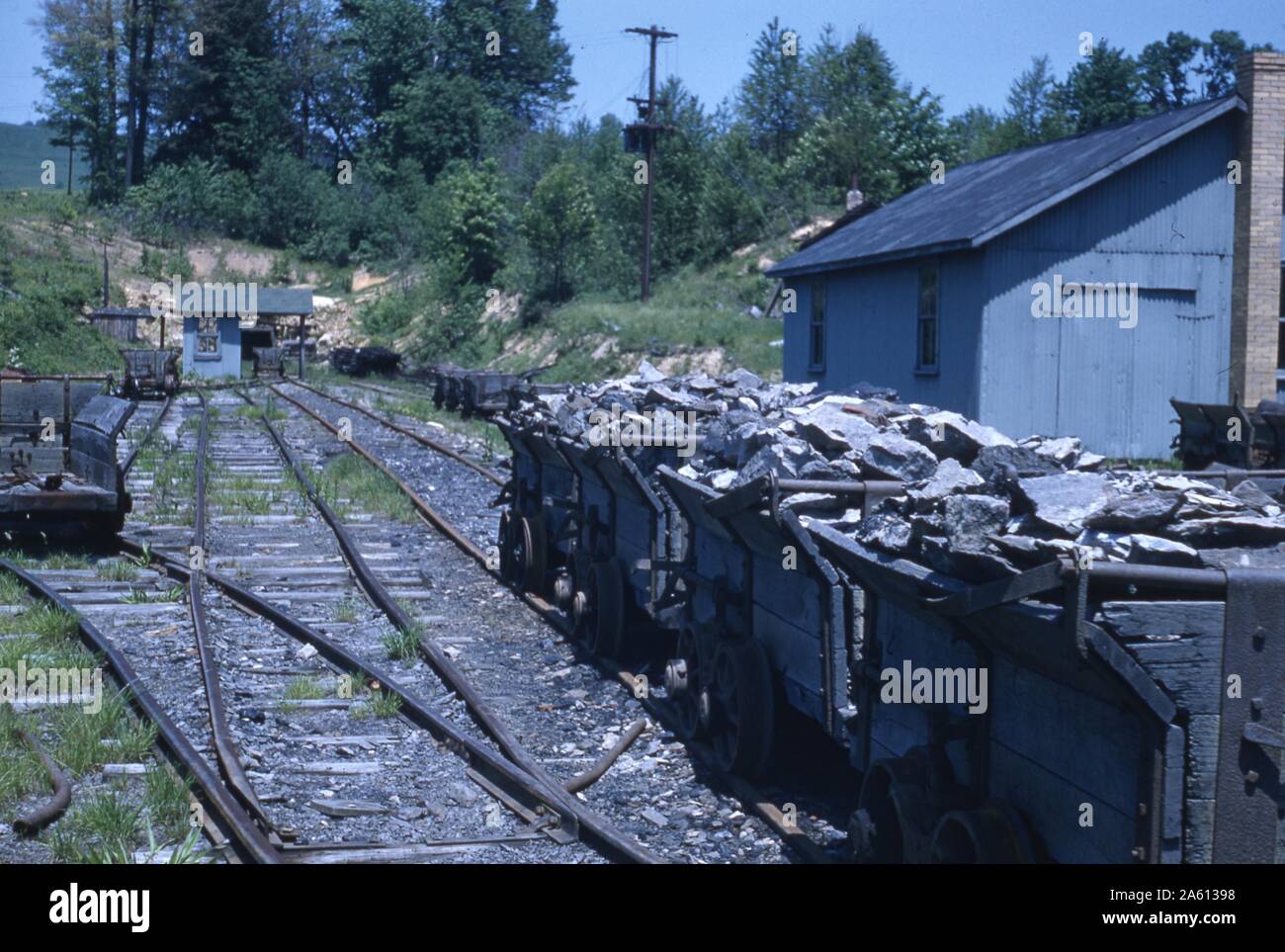 Plusieurs wagons de fret remplis de roches cassées s'assoient sur une voie d'évitement sur des voies ferrées près de bâtiments industriels, 1965. () Banque D'Images
