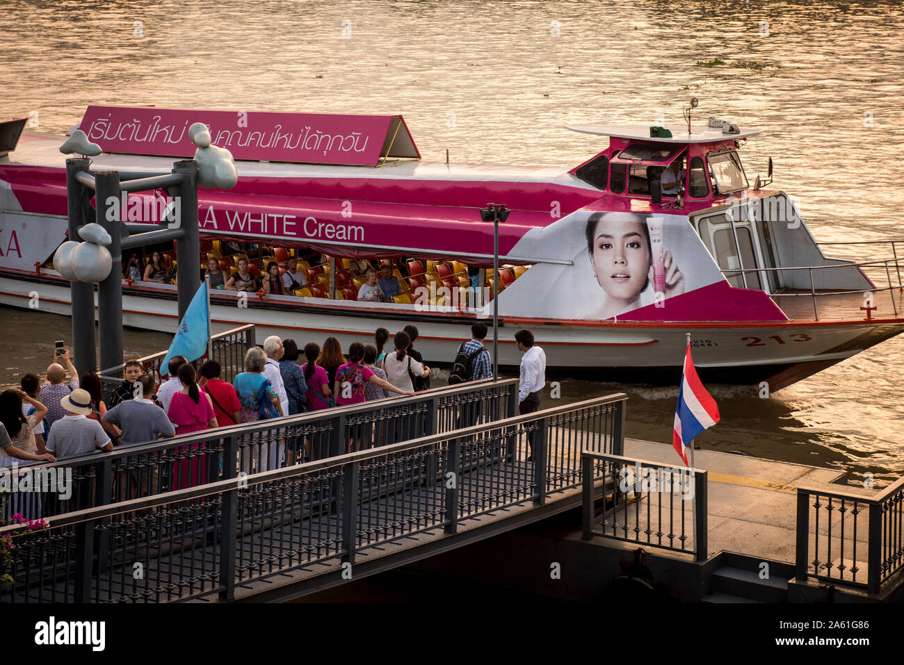 Les navetteurs et les touristes montent à bord d'un bateau-bus coloré sur le fleuve Chao Phraya de Bangkok, mêlant vie quotidienne, paysages urbains vibrants et couchers de soleil. Banque D'Images