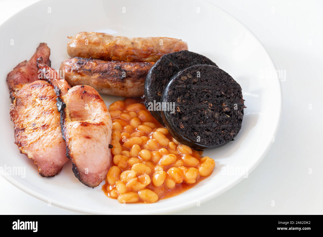 Saucisses de Cumberland, bacon, haricots blancs et du boudin noir dans un bol blanc Banque D'Images