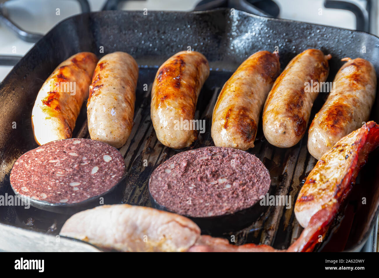 Saucisses de Cumberland, bacon, boudin noir la cuisson dans une crêpière pan Banque D'Images