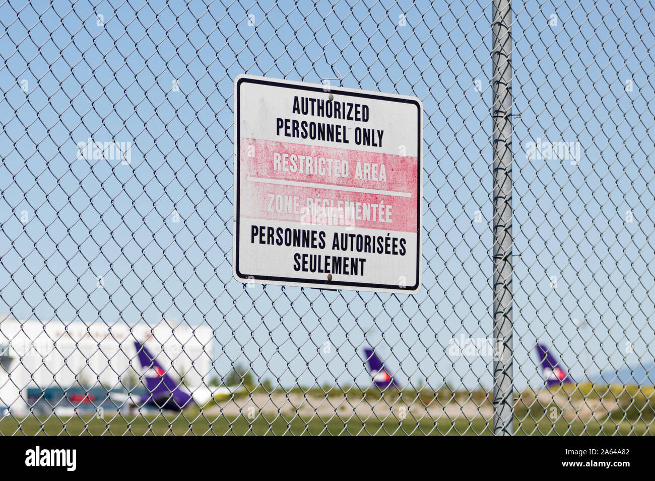 Personnel autorisé uniquement / zone restreinte - panneau français et anglais sur une clôture à l'extérieur de l'aéroport international de Vancouver. Aéroport avec avion en arrière-plan. Banque D'Images