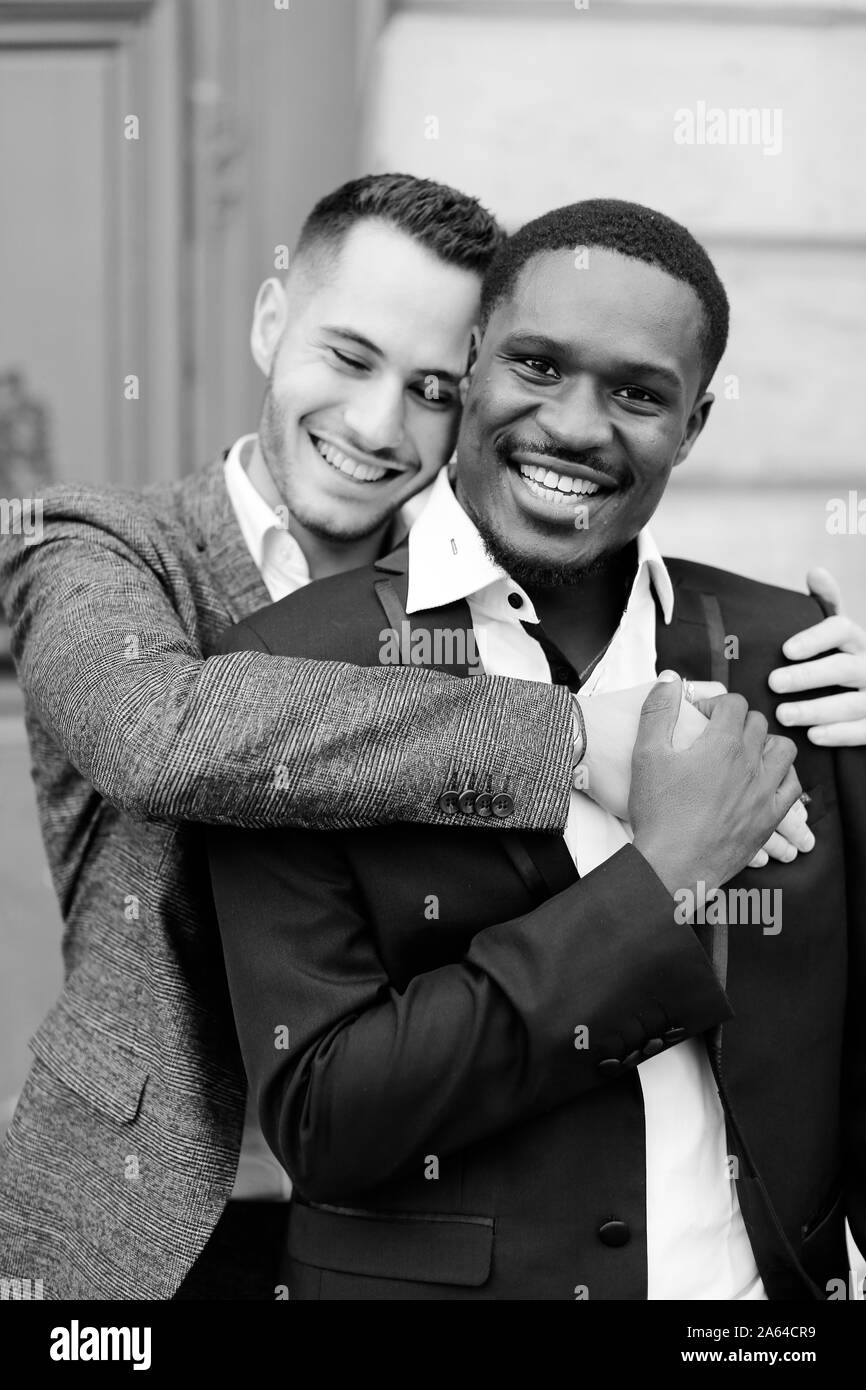 Portrait noir et blanc de deux hommes qui embrasent, caucasien et afro-américain, portant des costumes. Banque D'Images