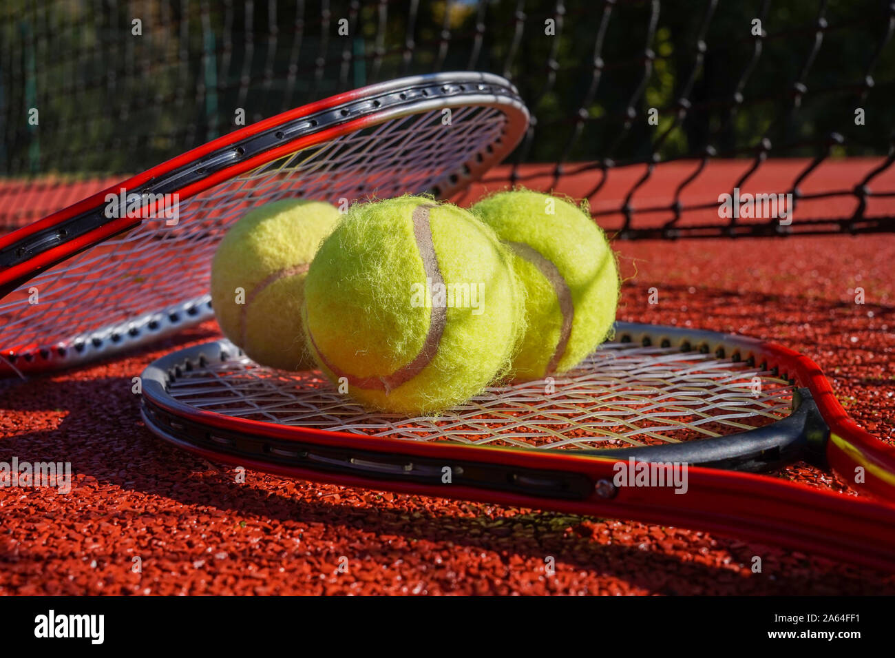 Scène de tennis avec filet noir d'ombre, des balles de tennis reposant sur une raquette de tennis sur surface dur rouge, low angle view, selective focus Banque D'Images