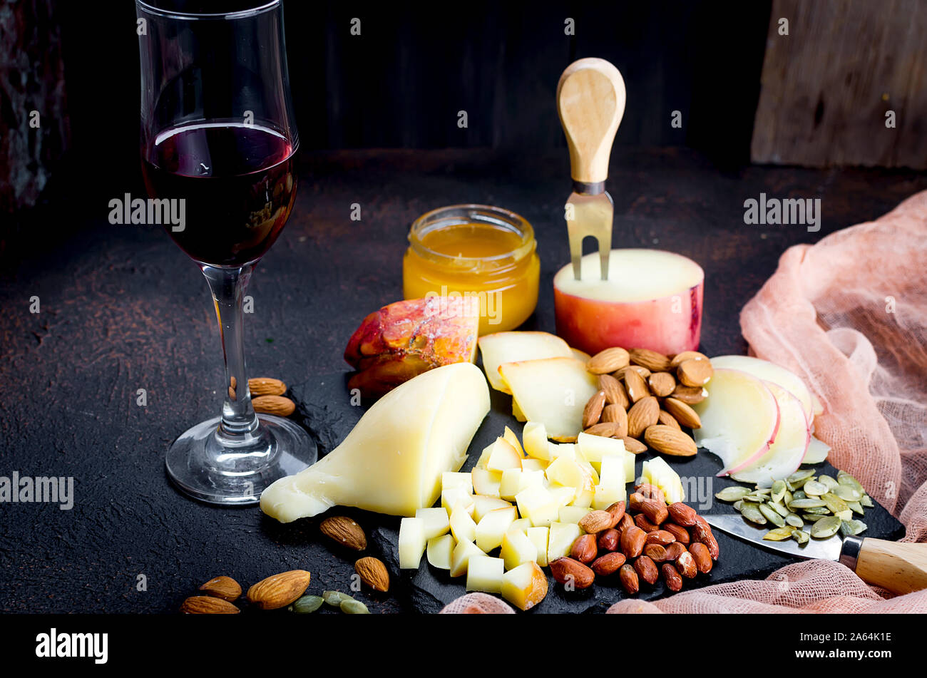 Verre de vin rouge, différentes variétés de fromage, d'amandes, miel en pot sur table en bois foncé Banque D'Images
