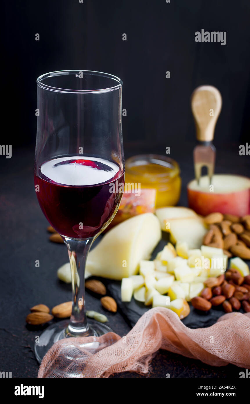 Verre de vin rouge, différentes variétés de fromage, d'amandes, miel en pot sur table en bois foncé Banque D'Images