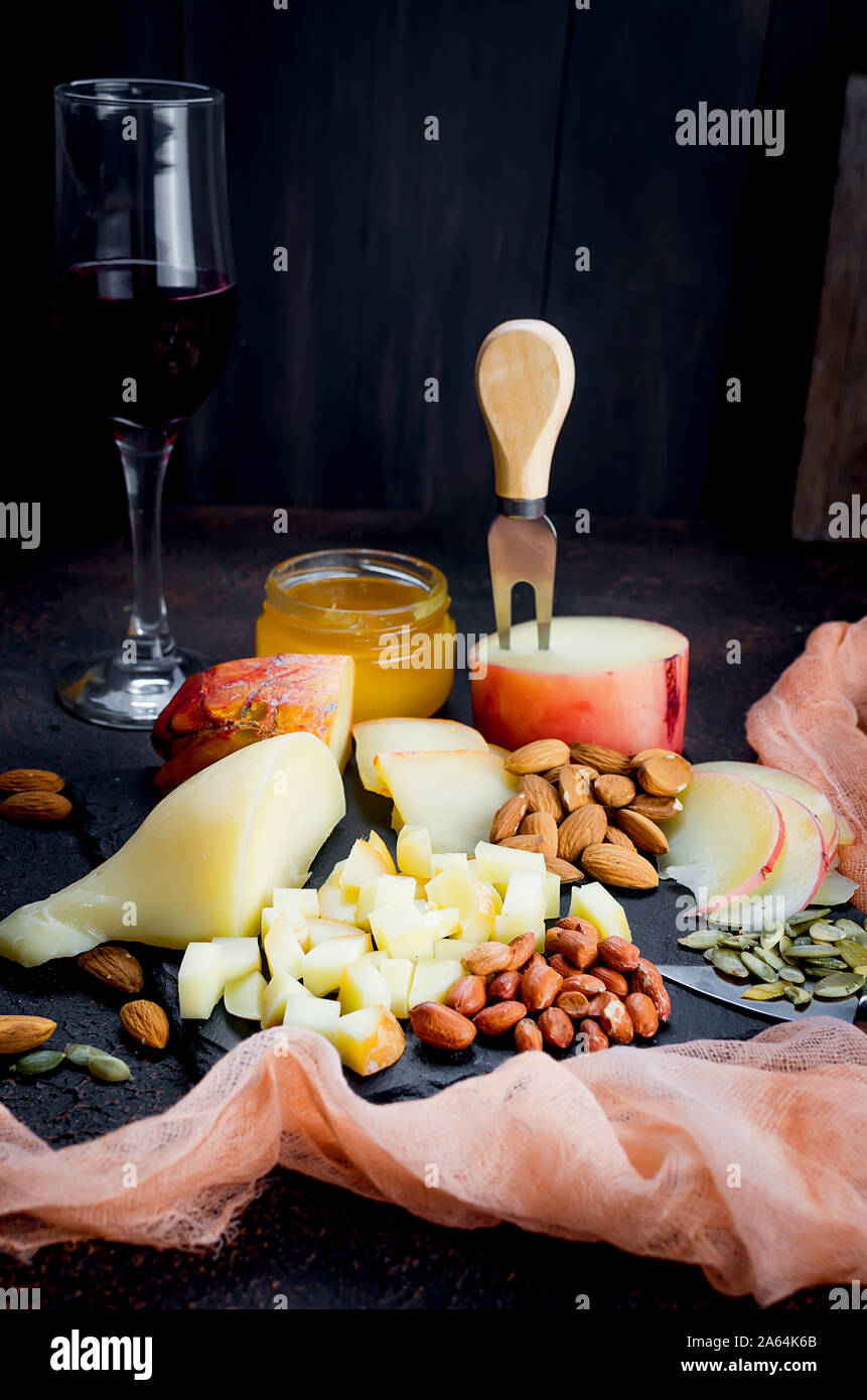 Verre de vin rouge, différentes variétés de fromage, d'amandes, miel en pot sur table en bois foncé Banque D'Images