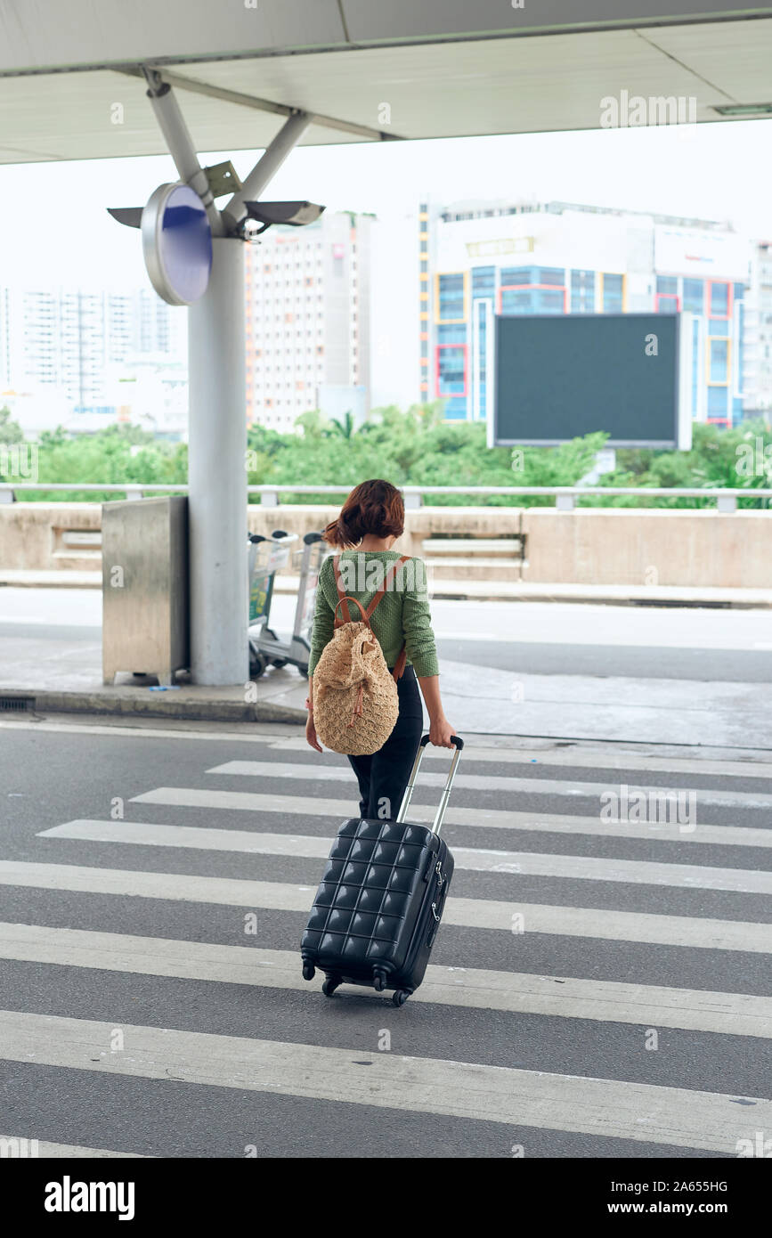 Asian female traveller traverser la route avec son rouleau valise à l'aéroport. Banque D'Images