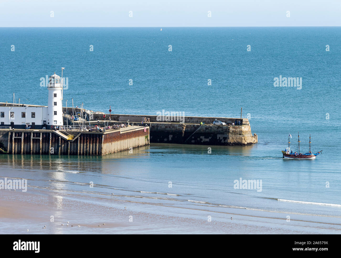 Le phare blanc au bout du port Pier et un bateau pirate qui se cap vers la mer à Scarborough North Yorkshire England Royaume-Uni Banque D'Images