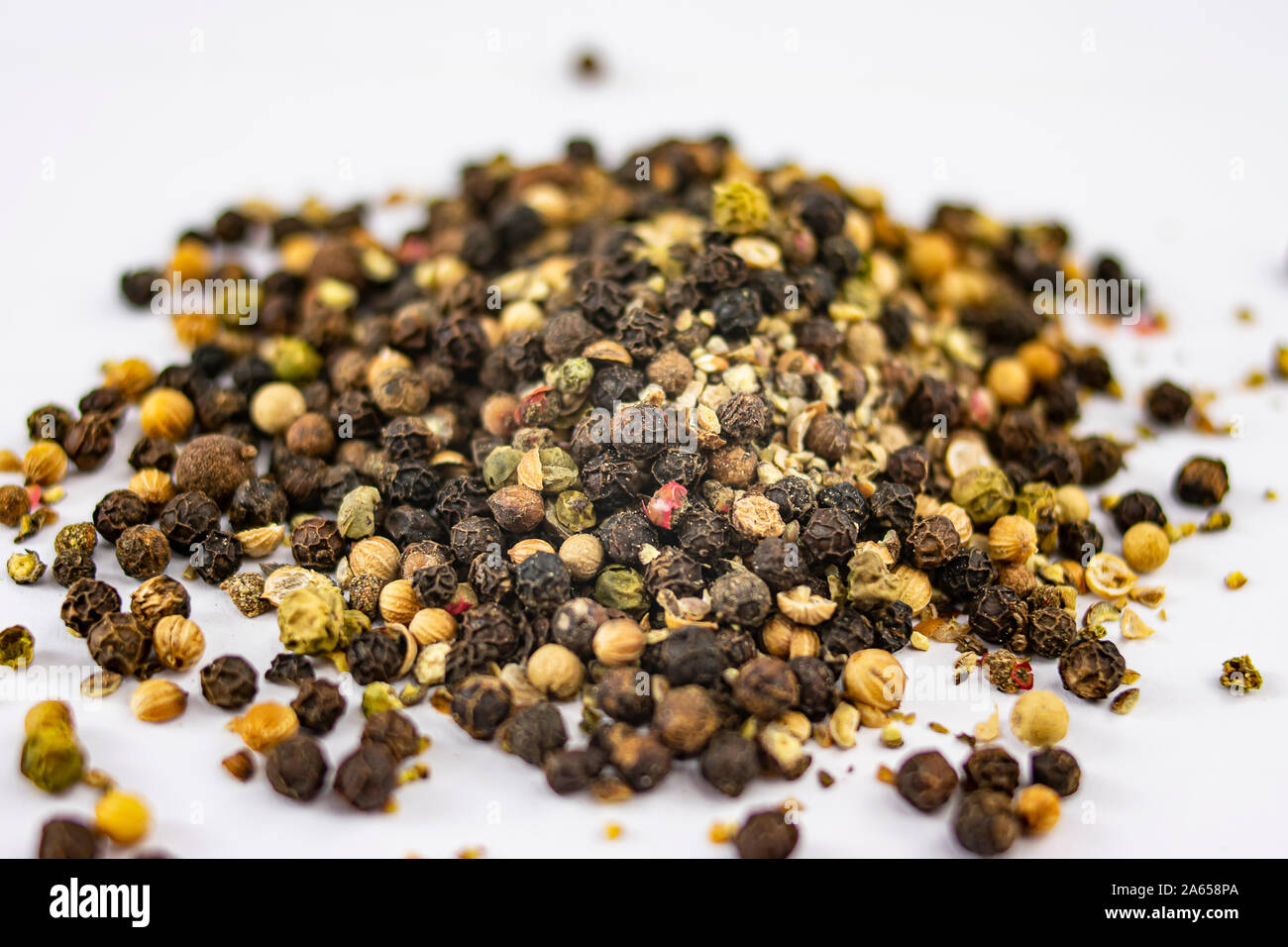 Tas de différents types de grains de poivre pour assaisonner les recettes de cuisine sur fond blanc Banque D'Images