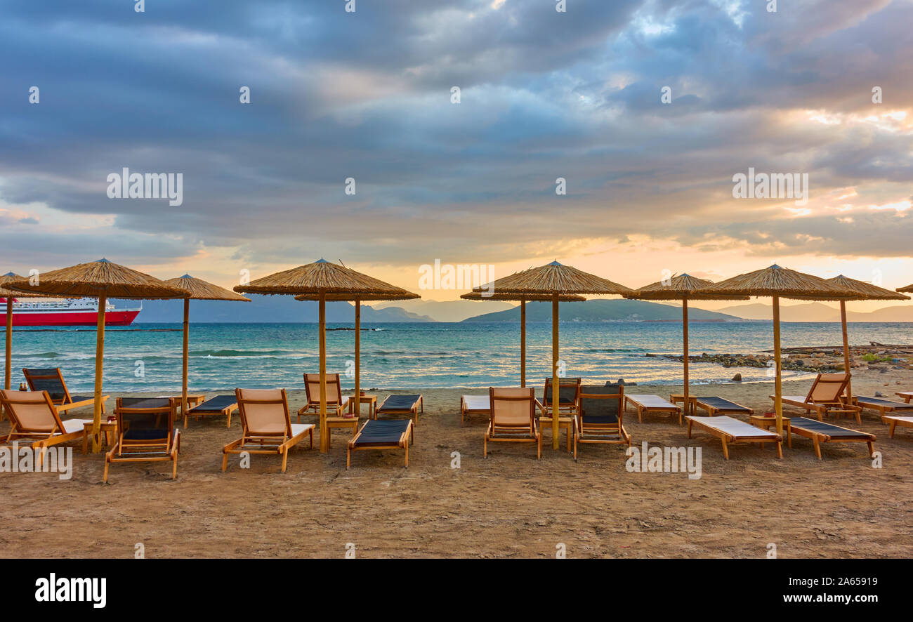 Panorana de plage vide avec chaises longues et parasols de paille par la mer et les nuages colorés au coucher du soleil, l'île d'Aegina, Grèce - Paysage - seasc Grec Banque D'Images