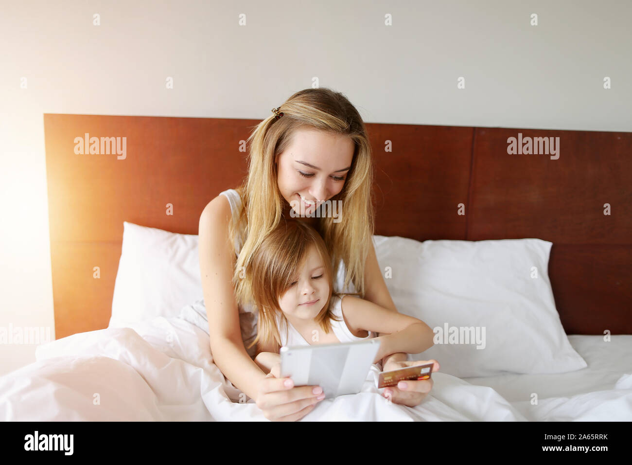 Portrait soleil mère et fille faire magasinage en ligne au lit blanc avec carte de crédit, votre tablette Banque D'Images