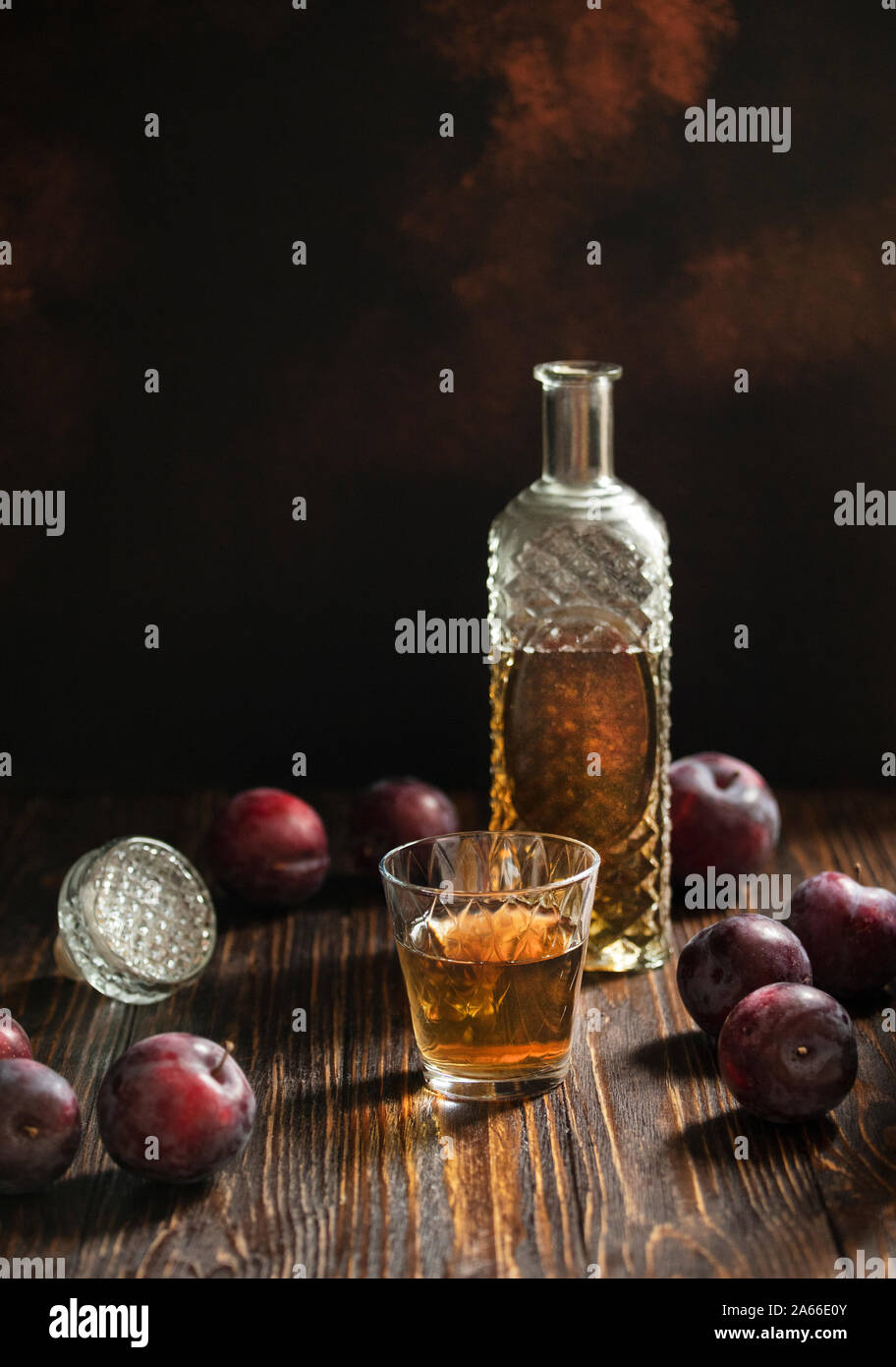 Rakia ou traditionnels de fruits brandy rakija des Balkans. Eau-de-vie de prune sljivovica dans un verre et la carafe sur une table en bois et un arrière-plan sombre. La verticale Banque D'Images