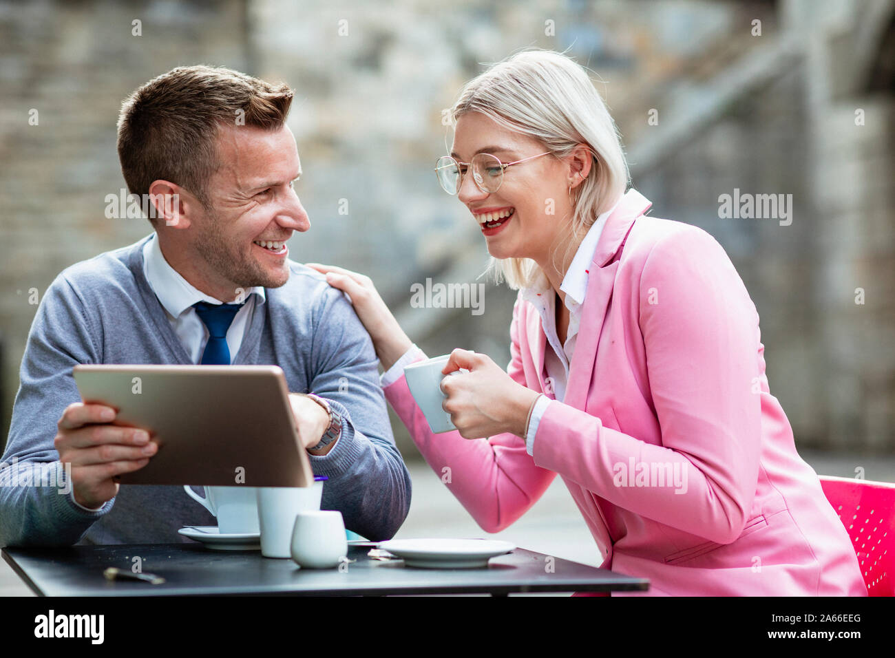 Deux entrepreneurs de s'asseoir et de rire de quelque chose sur une tablette numérique. La businesswoman holding est une boisson chaude et a sa main sur l'affaires Banque D'Images