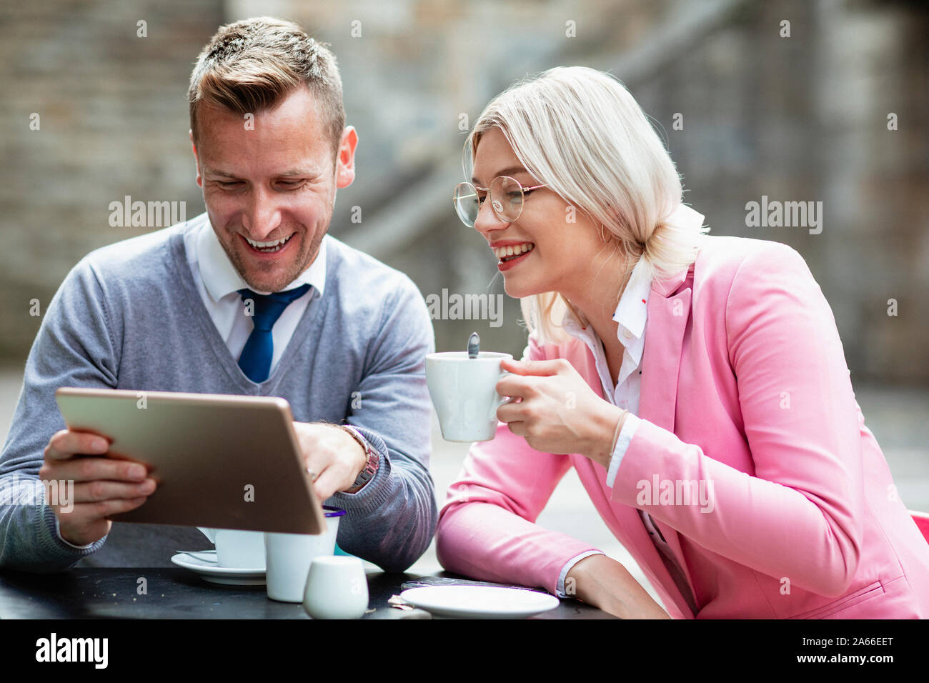 Deux entrepreneurs de s'asseoir et de rire de quelque chose sur une tablette numérique. La businesswoman holding est une boisson chaude, tandis que l'homme est titulaire d'e Banque D'Images