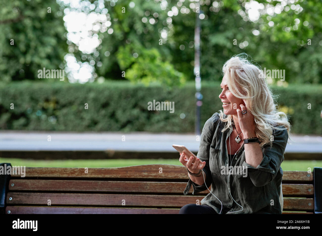 Une femme assise sur un banc de parc à l'écoute de la musique sur son lecteur MP3 tout en regardant sur le côté. Banque D'Images