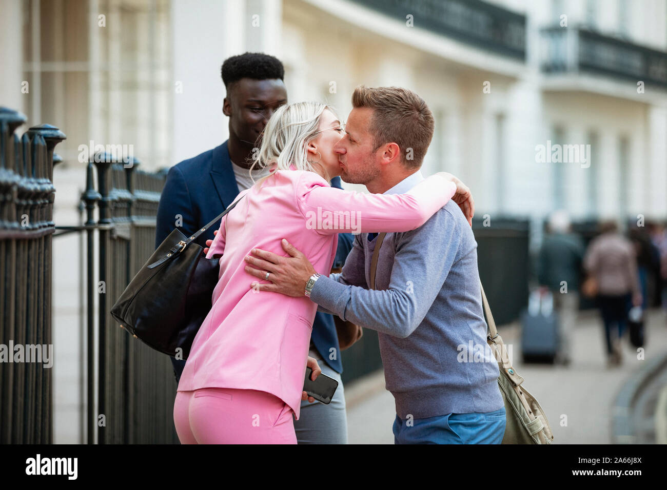 Deux hommes et une femme les collègues de travail de se rencontrer avant le travail d'accueil et de l'autre par un baiser sur la joue et Hug. Banque D'Images