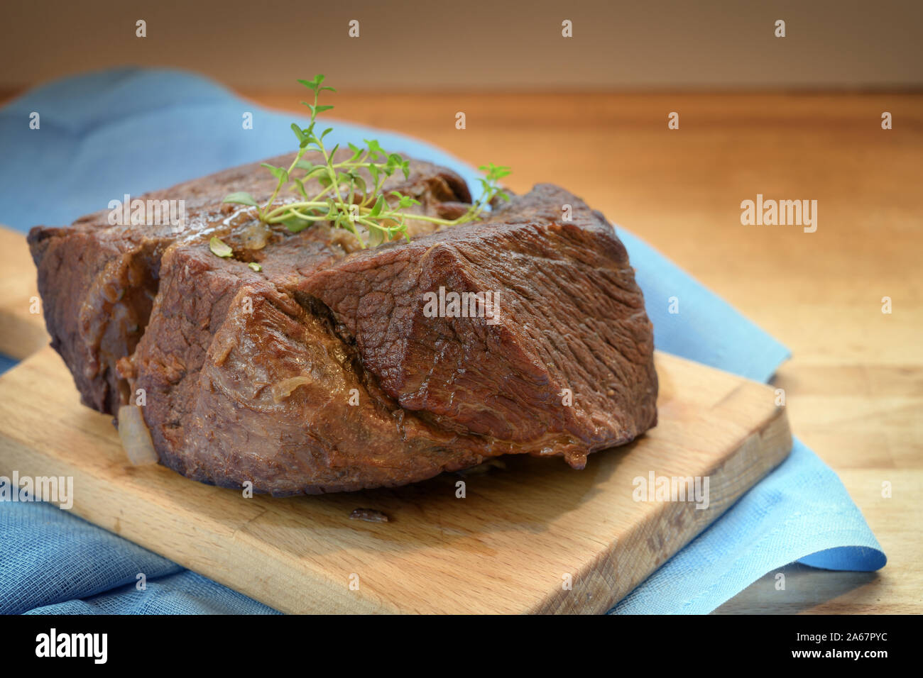 Rôti de bœuf braisé au thym garnir sur une planche en bois et d'une serviette bleue pour un dîner de fête comme le bœuf bourguignon, copie, espace de discussion sélectionné, nar Banque D'Images