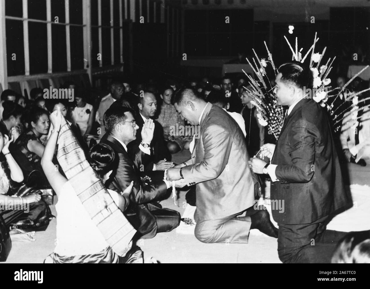 Un groupe d'hommes et de femmes habillés formellement s'assoit sur le sol, certains recevant des bracelets Sai Sin, lors d'une cérémonie Baci lors d'un événement commun pour l'armée américaine et l'armée royale thaïlandaise, photographié pendant la guerre du Vietnam, 1968. () Banque D'Images