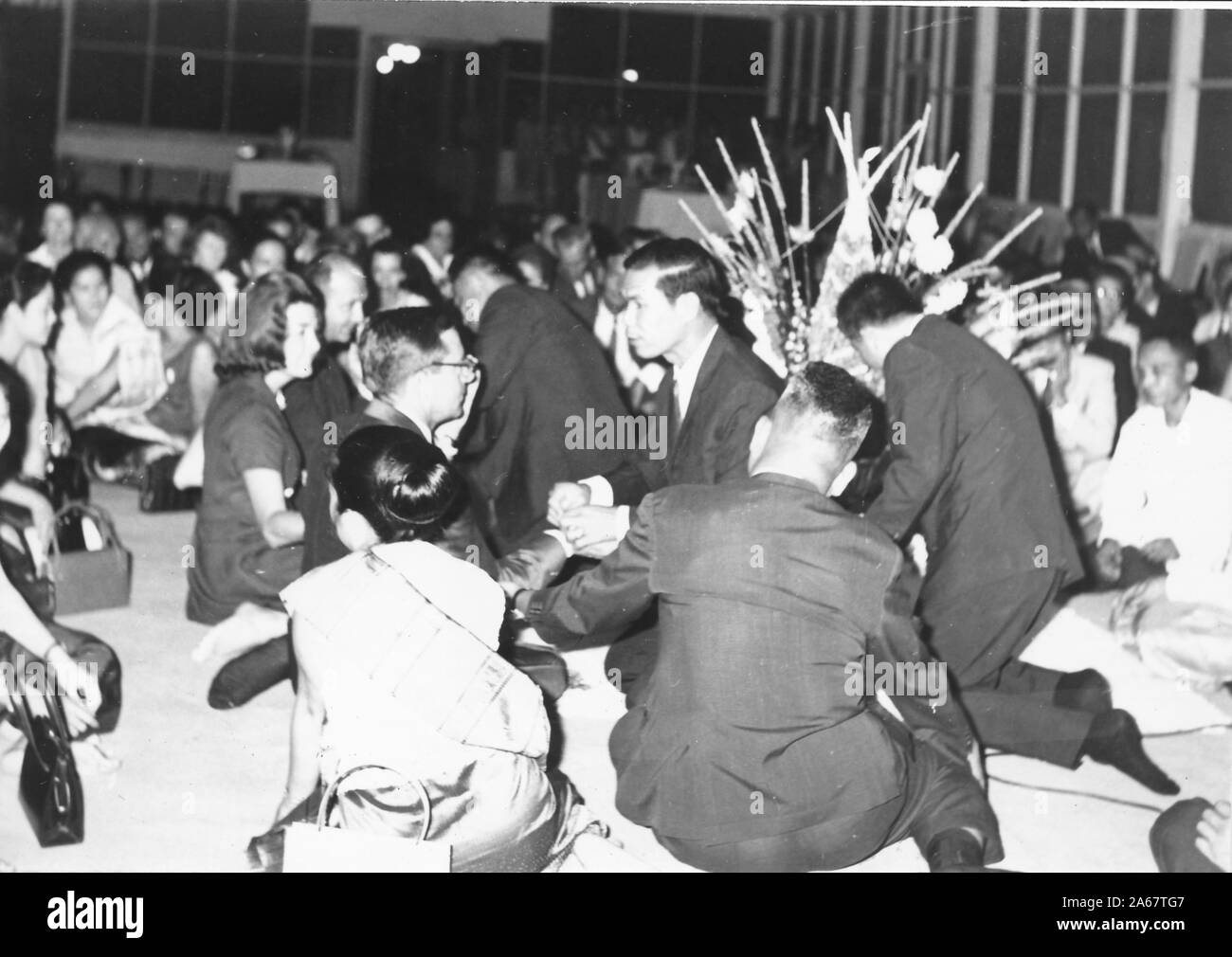 Un groupe d'hommes et de femmes habillés formellement s'assoit sur le sol, certains recevant des bracelets Sai Sin, lors d'une cérémonie Baci lors d'un événement pour l'armée américaine et l'armée royale thaïlandaise, photographié pendant la guerre du Vietnam, 1968. () Banque D'Images