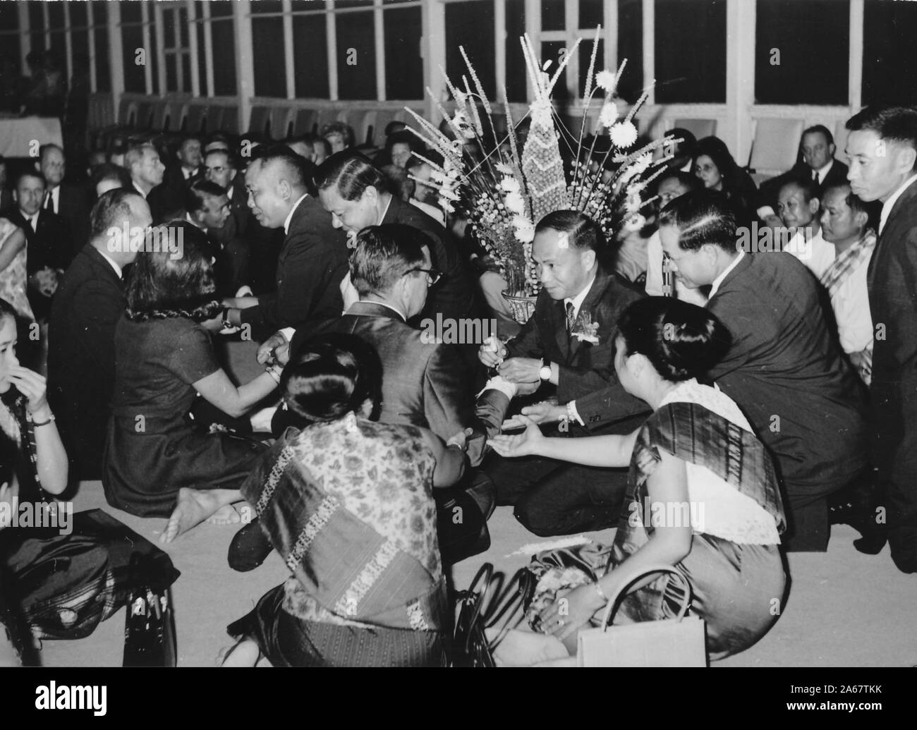Un groupe d'hommes et de femmes habillés formellement s'assoit sur le sol, certains recevant des bracelets Sai Sin, lors d'une cérémonie Baci à une fonction conjointe de l'armée américaine et de l'armée royale thaïlandaise, photographiée pendant la guerre du Vietnam, 1968. () Banque D'Images