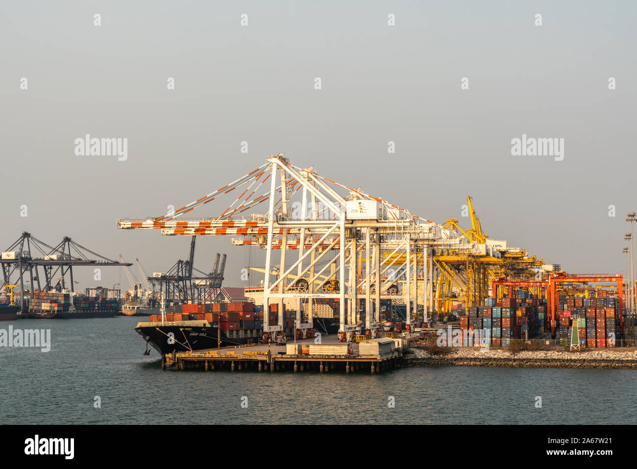 Port de Laem Chabang, Thaïlande - Mars 17, 2019 : longue vue sur un grand nombre de grues sur le quai avec des piles de boîtes colorées contre la lumière blu Banque D'Images