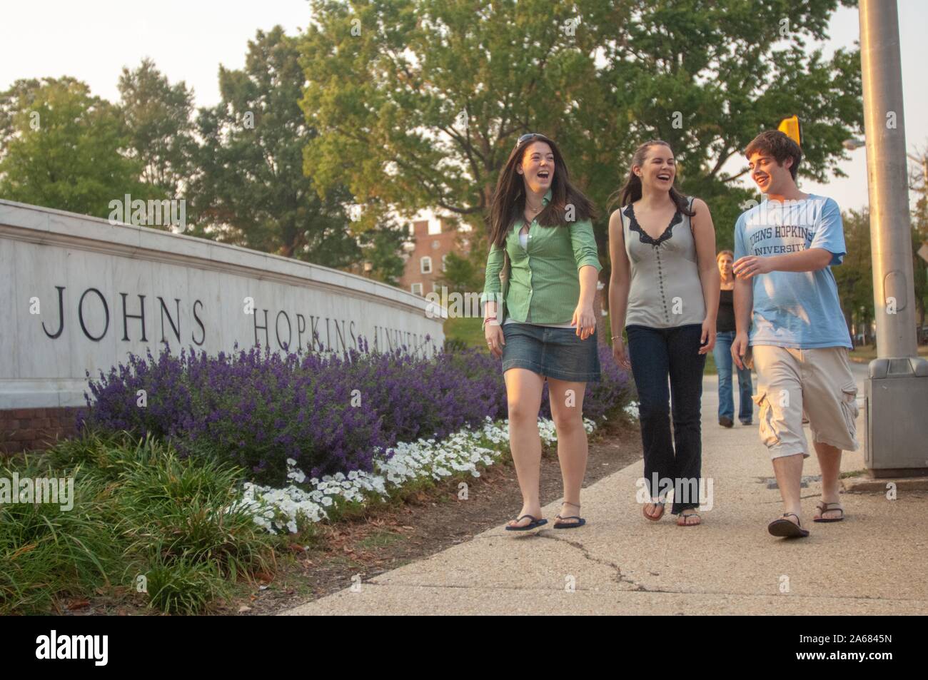 Tir à faible angle de trois étudiants, en riant lorsqu'ils marchent le long d'un trottoir, devant un panneau en béton bas gravé avec les mots 'Johns Hopkins University, ' Baltimore, Maryland, 26 septembre 2007. De La Homewood Photography Collection. () Banque D'Images