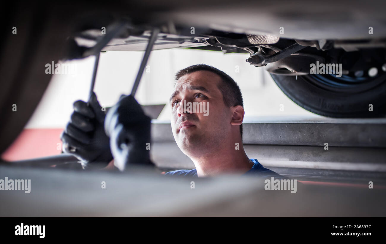 Mécanicien réparateur automobile Maître technicien de contrôle de l'état sous la voiture, sur l'ascenseur du véhicule en atelier Banque D'Images