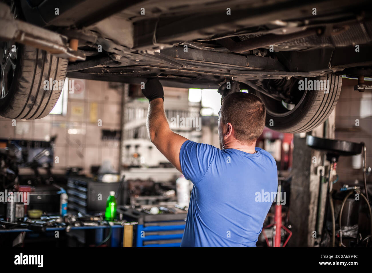Mécanicien réparateur automobile Maître technicien de contrôle de l'état sous la voiture, sur l'ascenseur du véhicule en atelier Banque D'Images