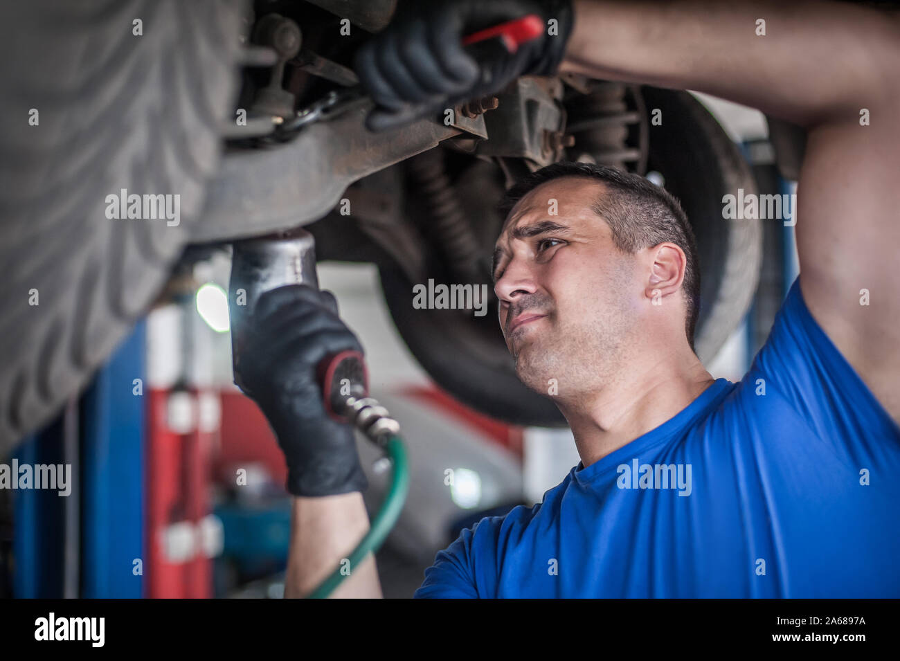 Mécanicien réparateur automobile Maître technicien de contrôle de l'état sous la voiture, sur l'ascenseur du véhicule en atelier Banque D'Images