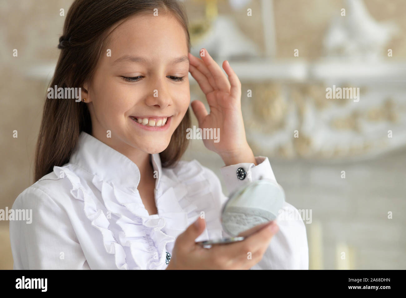 Smiling little girl en blouse blanche à la recherche de petit miroir Banque D'Images