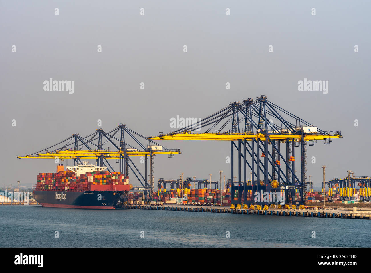 Port de Laem Chabang, Thaïlande - Mars 17, 2019 : Grand HAPAG-LLOYD blue container ship travaillé par de hautes grues bleu et jaune sous Ciel de coucher du soleil. De Pont Banque D'Images