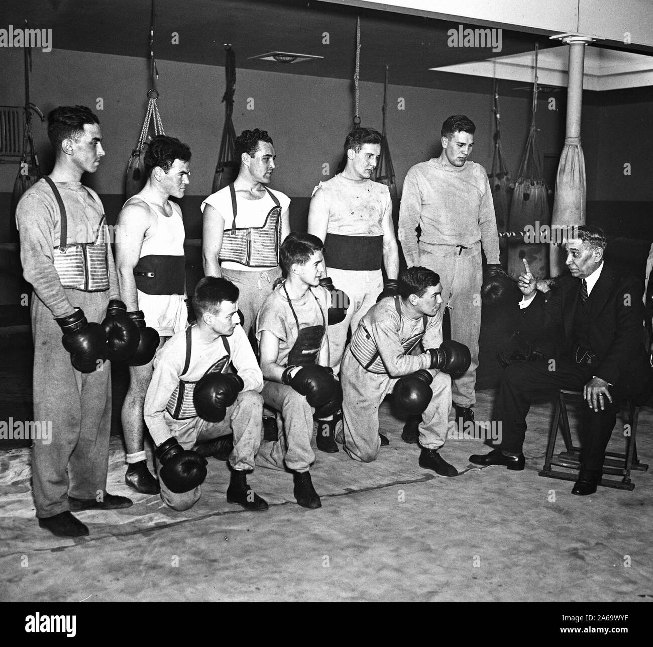 Un homme parle à un groupe de boxeurs dans un club de boxe, peut-être un entraîneur ca. 1936 Banque D'Images