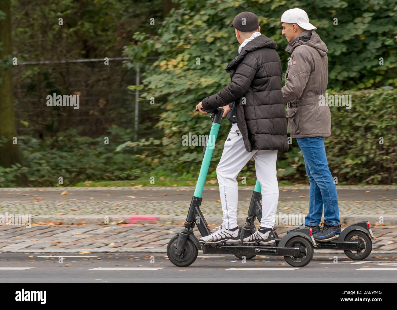 Deux garçons sur les scooters électriques filmé avec effet panoramique en mouvement sur un fond de plantes vertes Banque D'Images