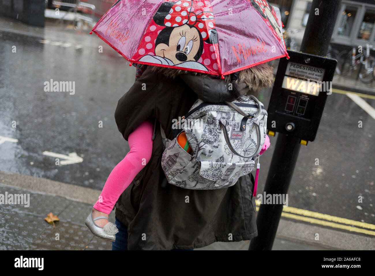 Une mère porte son enfant sous un parapluie Minnie Mouse au cours de fortes pluies sur une après-midi d'automne près de Trafalgar Square, le 24 octobre 2019, à Westminster, Londres, Angleterre. Banque D'Images