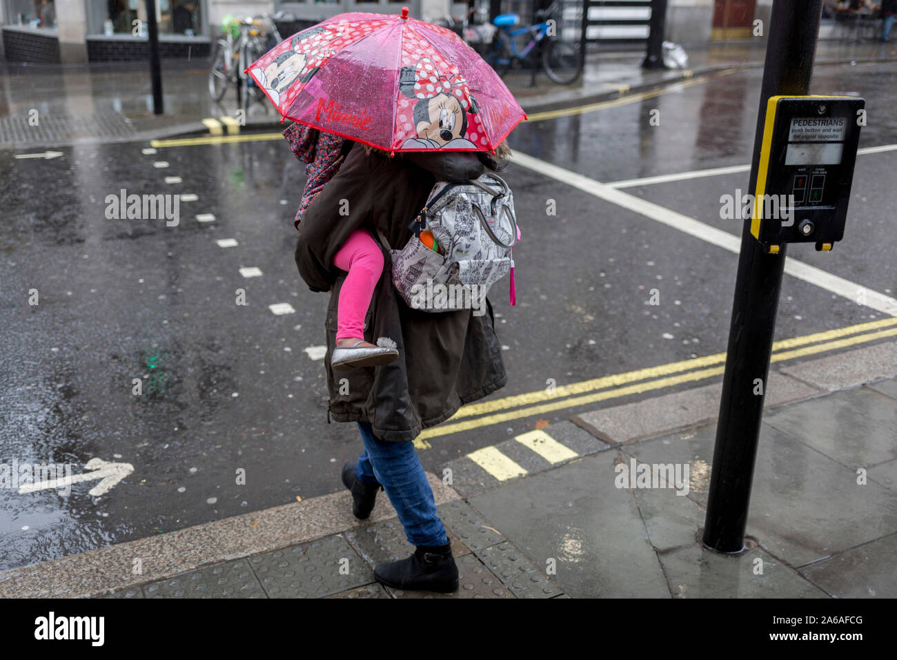 Une mère porte son enfant sous un parapluie Minnie Mouse au cours de fortes pluies sur une après-midi d'automne près de Trafalgar Square, le 24 octobre 2019, à Westminster, Londres, Angleterre. Banque D'Images