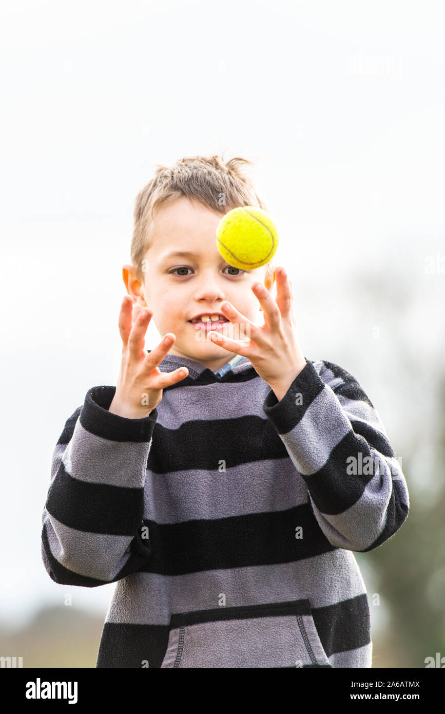 Un beau petit garçon avec le TDAH, l'Autisme, syndrome d'Aspergers attraper ses pratiques de coordination avec une balle de tennis dans le parc, tennis coaching Banque D'Images