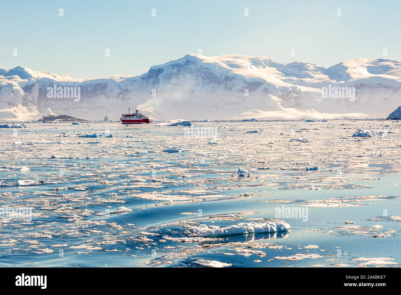 Croisière rouge dérive vapeur loin parmi les icebergs à l'énorme rocher et des glaciers en arrière-plan, la baie de Neco, Antarctique Banque D'Images