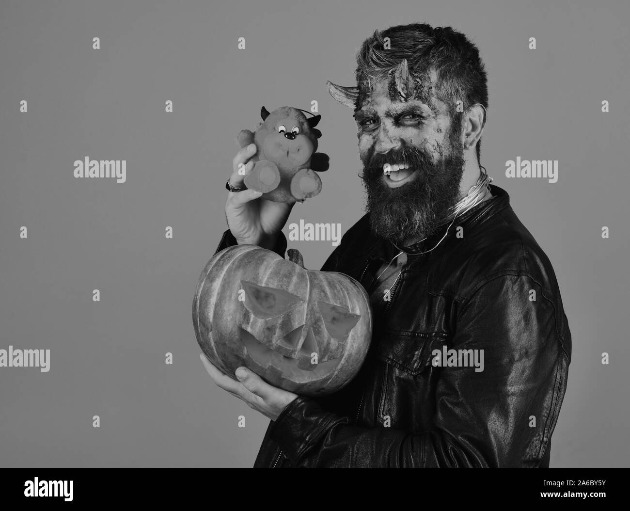 Homme portant un miroir effrayant détient la citrouille et la diable rouge jouet sur fond bleu. Monster avec décorations d'octobre. Halloween party concept. Démon avec des cornes et sourire sculpté détient jack o lantern Banque D'Images