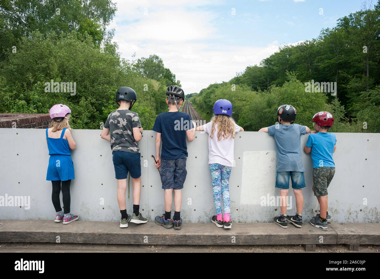 Un groupe d'enfants se tiennent sur un pont en attendant et regardant un train sur les pistes. Banque D'Images