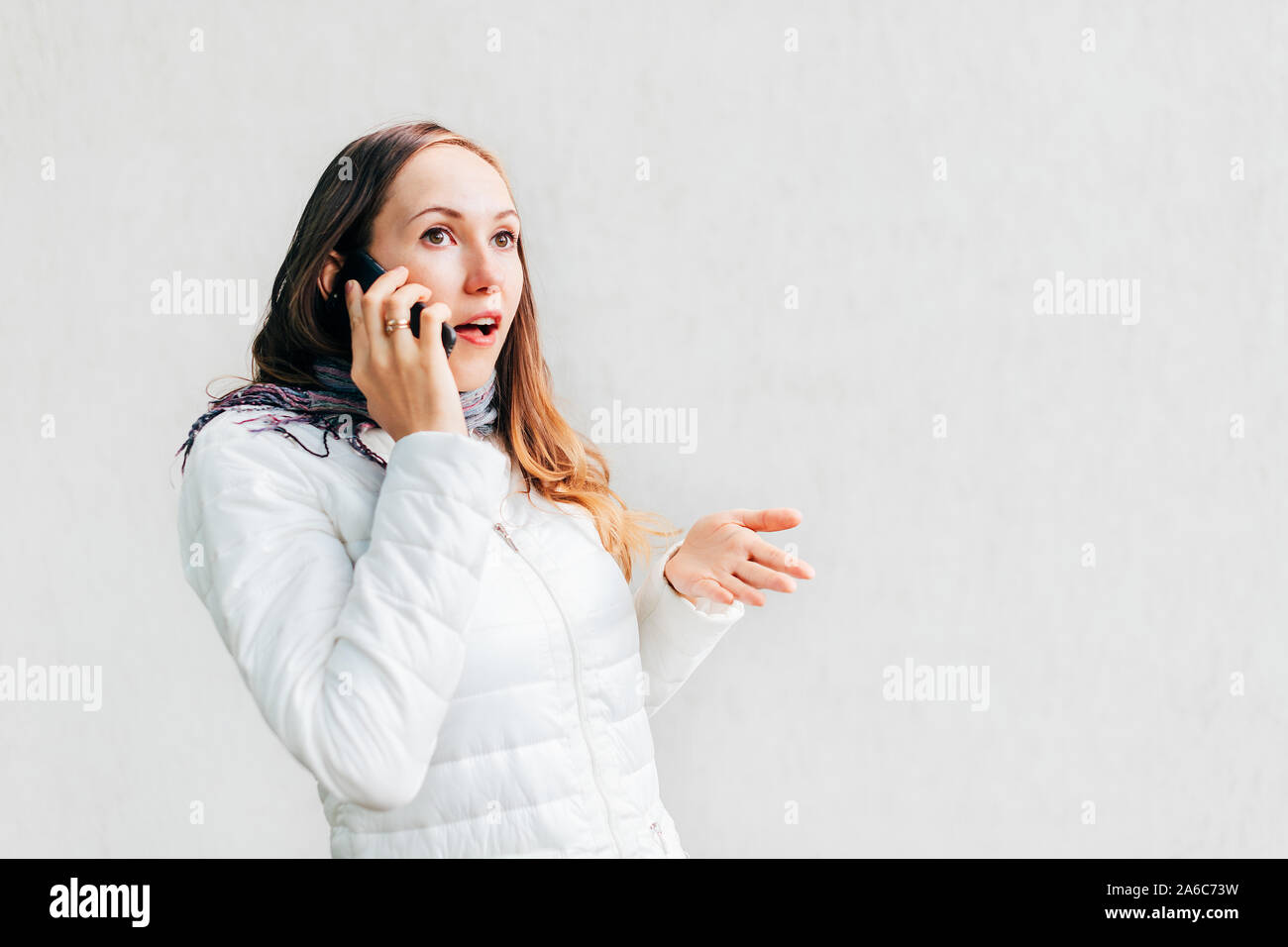 Portraitof young Caucasian woman with brunette avec enthousiasme de cheveux gesticuler arguant sur téléphone mobile sur mur monochrome d'arrière-plan. Banque D'Images