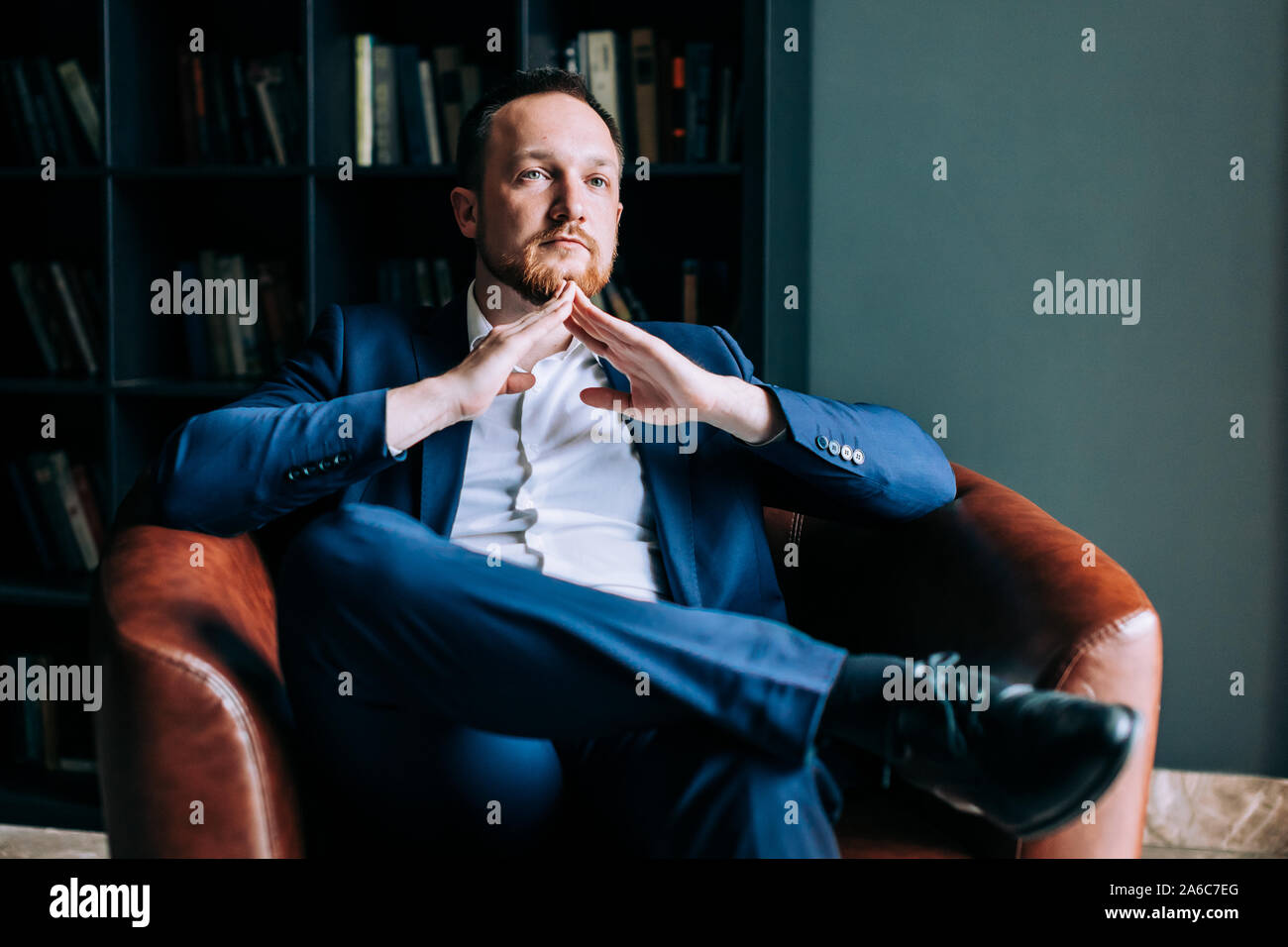 Des profils d'affaires réussi dans un costume est assis dans sa chaise avec les bras croisés. Banque D'Images